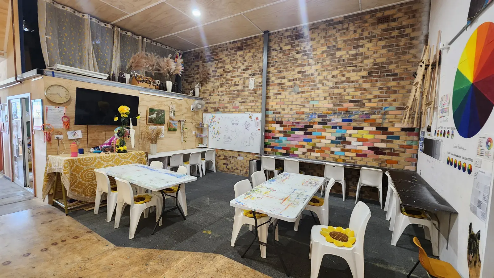 Wide view across the art studio showing tables, painted brick wall and colour wheel mural